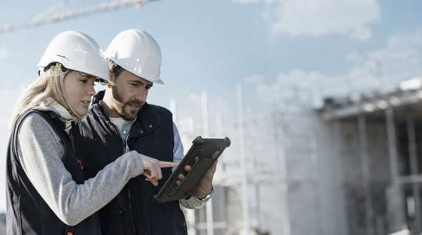 A modern construction site with workers using AI-powered tablets and holographic displays for project management, highlighting efficiency and advanced technology.